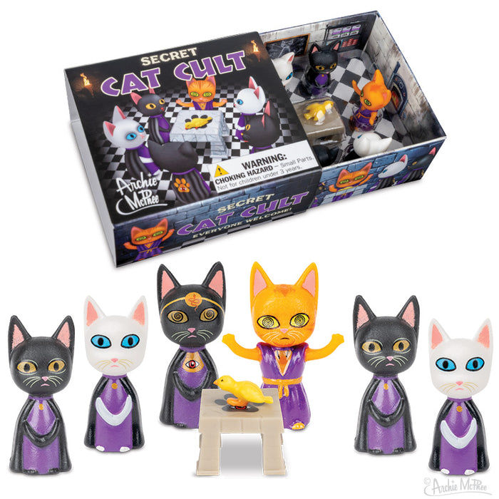 Six toy cat figurines dressed in cult robes surrounding an altar with a bird on it with a matchbox style package in the background.