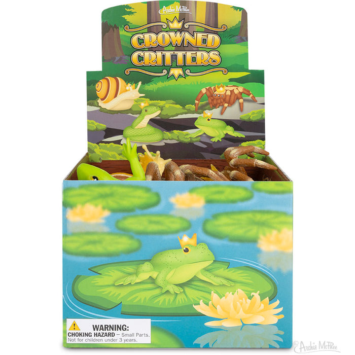 Colorful display box of Crowned Critters toys featuring whimsical pond animals wearing crowns, including a green frog on a lily pad, snail, spider, and snake, suitable for children over 3 years old