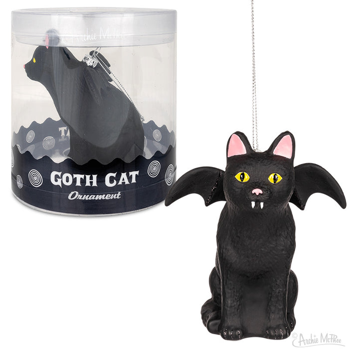 Black cat ornament with bat wings and fangs, sitting upright. Yellow eyes and pink inner ears. Cylindrical packaging with "Goth Cat Ornament" label visible. Hanging string attached for tree display.