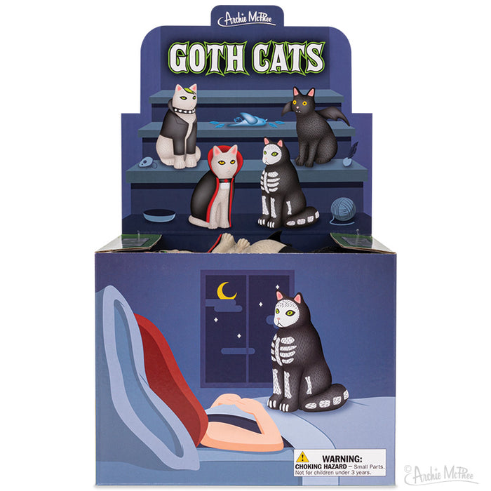 Goth Cats display box featuring four unique vinyl cat figurines in gothic styles, showcasing different designs on a tiered shelf with spooky nighttime scene on the box front, perfect for Halloween decor or year-round gothic enthusiasts