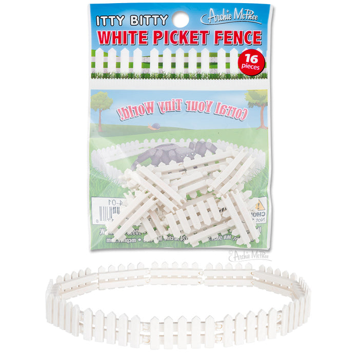 Miniature white picket fence toy in packaging, showing small fence pieces and assembled circular fence example. Product title and colorful suburban background visible on package.