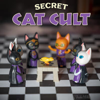 Six toy cat figurines dressed in cult robes surrounding an altar on.a checkerboard floor with the words "Secret Cat Cult" above.