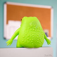 Green textured toy frog on a white surface with a blurred background