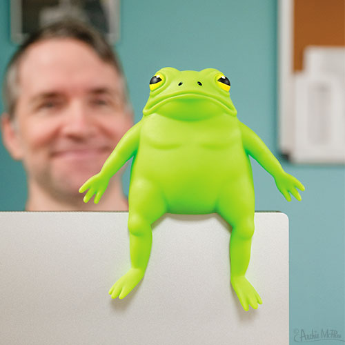 Green frog toy on a surface with a blurred person in the background