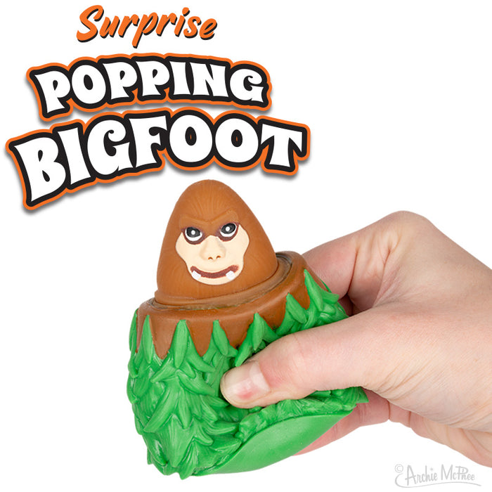 Surprise Popping Bigfoot toy with brown creature emerging from green forest base, held by hand. Orange and white text logo above.