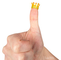 Tiny golden crown perched on an upright thumb, demonstrating the miniature size of Itty Bitty Crowns. Perfect for transforming action figures or toys into royalty.