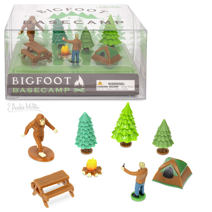 Bigfoot Basecamp miniature playset with tiny figures including Bigfoot, camper, trees, tent, picnic table, and campfire in a display box, alongside individual pieces arranged below