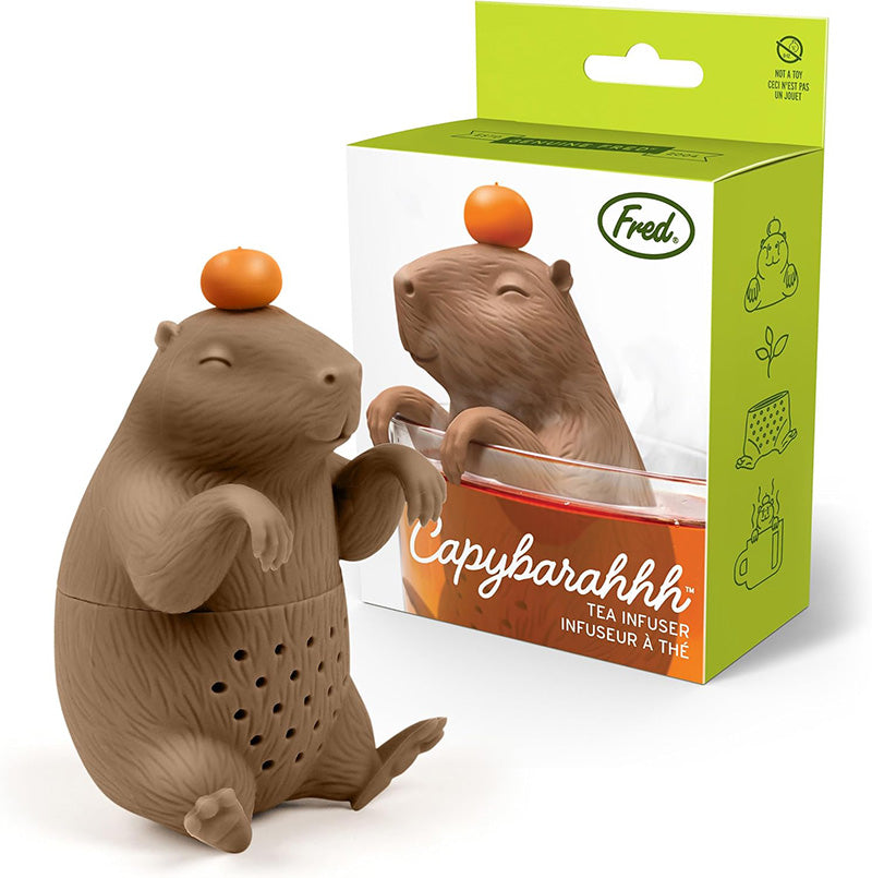 A brown capybara-shaped tea infuser with a small orange on its head and the package in the background