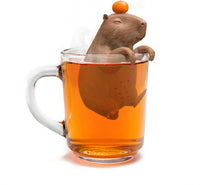 A brown capybara-shaped tea infuser with a small orange on its head sitting in a clear cup of tea