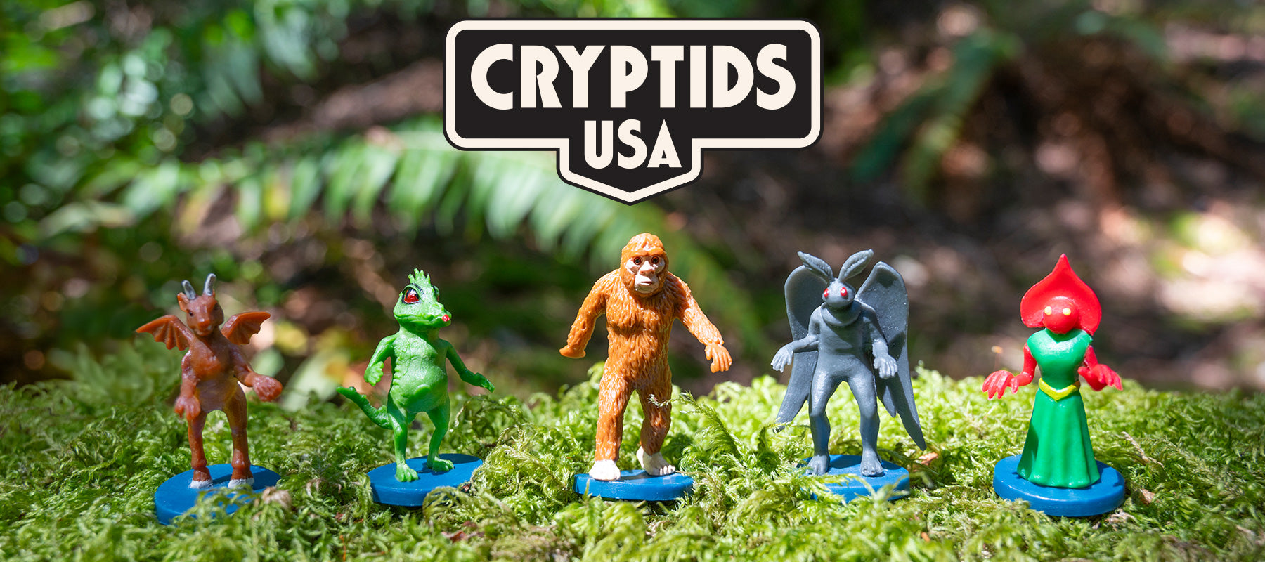 Five cryptid figurines stand on moss under a Cryptids USA sign.