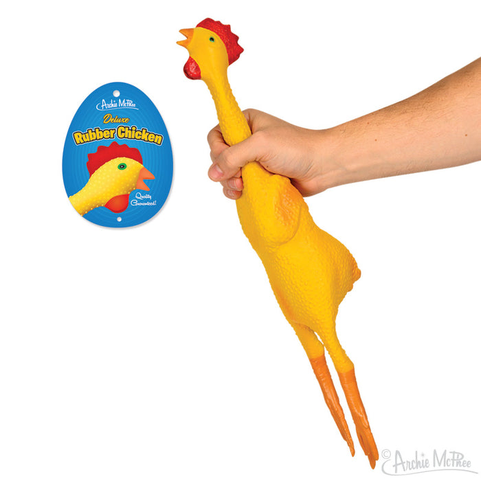 Deluxe Rubber Chicken toy held by hand, showcasing its bright yellow color and elongated neck. Product packaging visible with blue background and rubber chicken image. Humorous novelty item for entertainment and pranks.