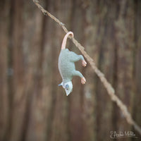 A charming Itty Bitty Possums toy lemur dangles upside down from a rope against a blurred forest background, embodying the adventurous spirit of its leafy realm.