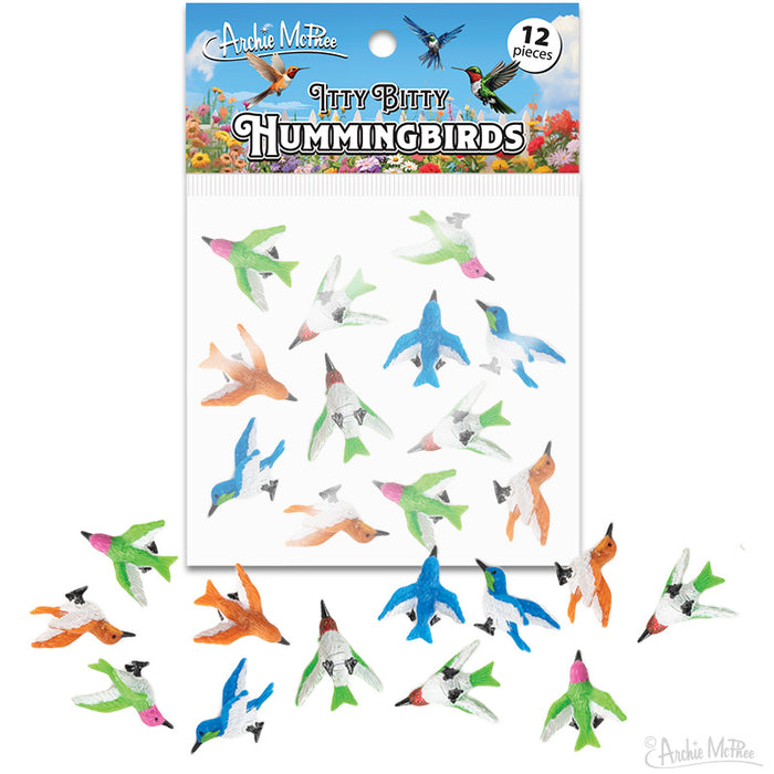 Colorful miniature hummingbird figurines in various poses and vibrant colors, packaged in a set of 12 pieces. Product image shows tiny vinyl birds scattered around the packaging, illustrating the diverse designs and playful nature of the Itty Bitty Hummingbirds collection.