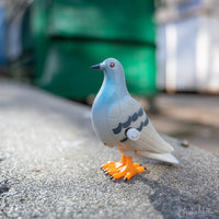 Perky Pigeon Wind-up toy scene on pavement with a dumpster in the background