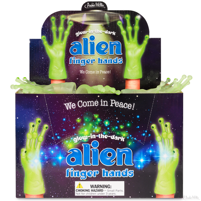 Glow-in-the-dark alien finger hands display box featuring bright green, three-fingered hands against a starry space background. Product title and "We Come in Peace!" message visible on colorful packaging.