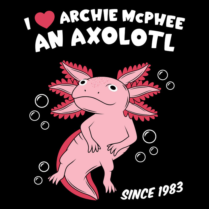 Pink axolotl cartoon on black t-shirt with text "I heart Archie McPhee an Axolotl" and "Since 1983". Cute amphibian with feathery gills surrounded by bubbles, smiling.