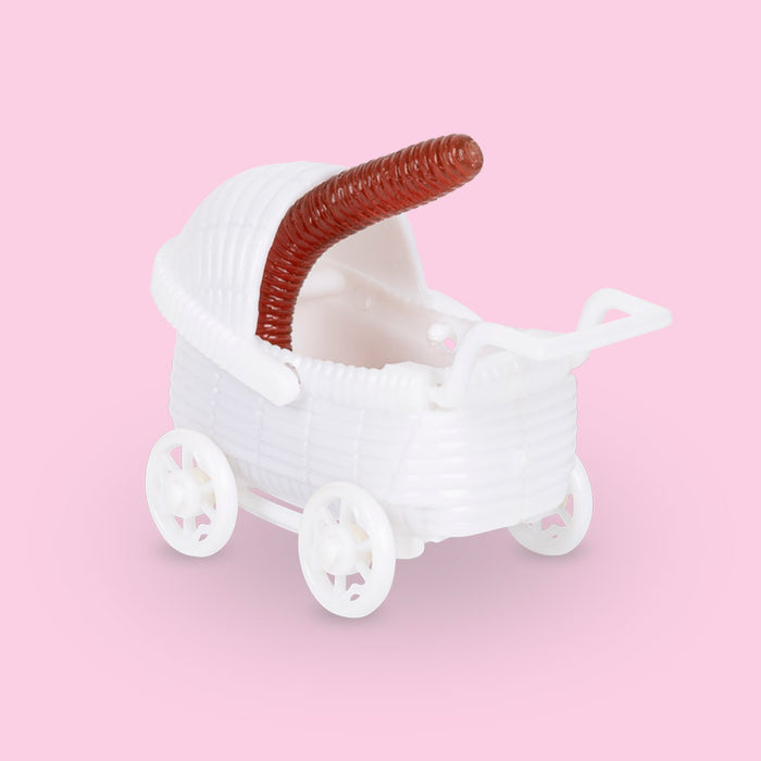 Adorable Baby Worm toy in miniature white baby carriage, featuring a reddish-brown worm peeking out from the stroller against a soft pink background. Unique and whimsical product for children or collectors.