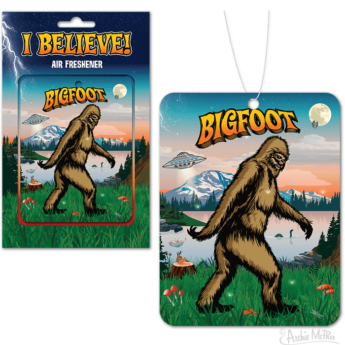 Bigfoot-themed air freshener with colorful packaging and hanging card design, featuring a sasquatch walking in a forest landscape with mountains, UFO, and full moon in the background