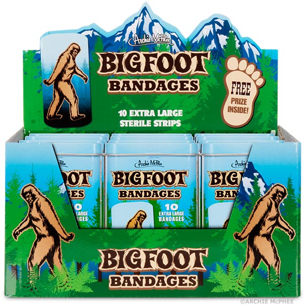 Display box of Bigfoot Bandages featuring mountain scenery, Bigfoot illustrations, and multiple tins of bandages. Each tin advertises 40 extra large sterile strips and a free prize inside. The box showcases the product's branding and design.