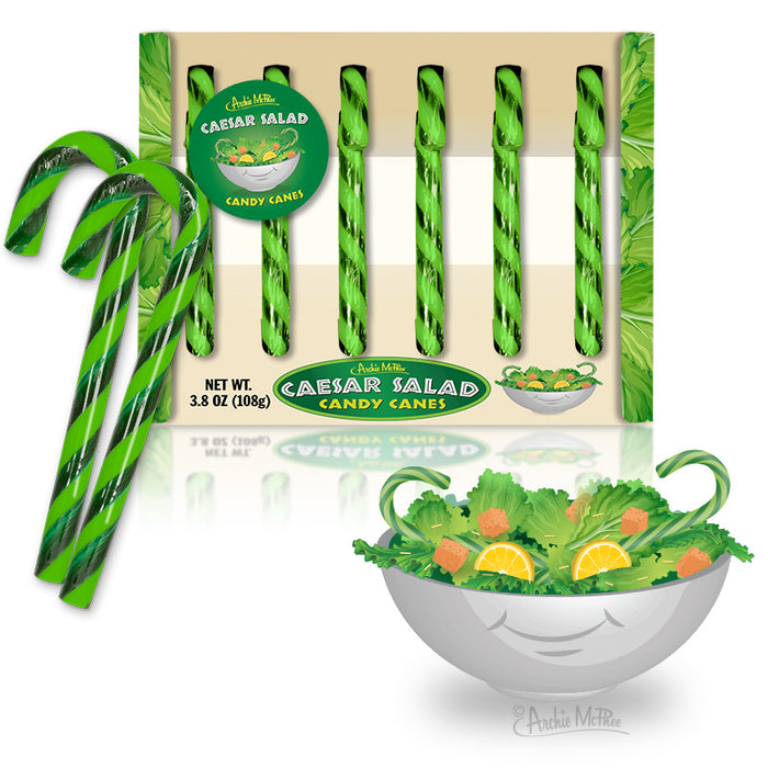 Caesar Salad Candy Canes in green and white stripes displayed in packaging with product label. Six candy canes visible, alongside illustrated Caesar salad bowl. Unique holiday treat combining sweet candy with savory salad flavors.