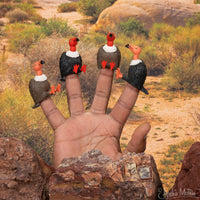 four vulture finger puppets on a hand in a desert setting