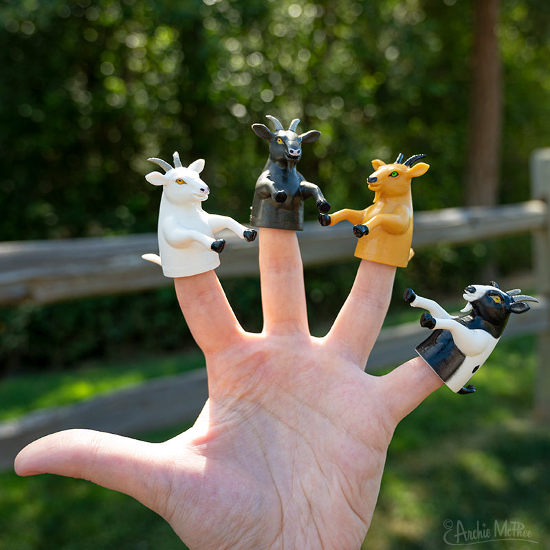 four goat finger puppets on a hand in an outdoor setting