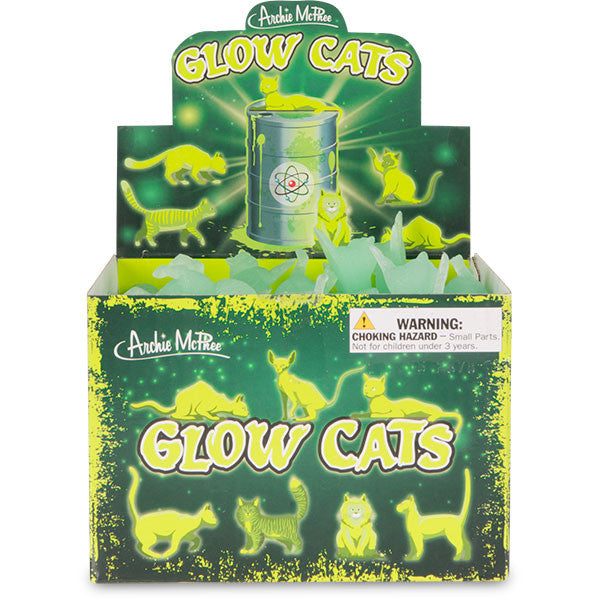 Colorful display box showcasing Glow Cats, featuring luminescent cat figurines in various poses surrounding a central container. Product packaging highlights the glow-in-the-dark feature and includes a choking hazard warning.