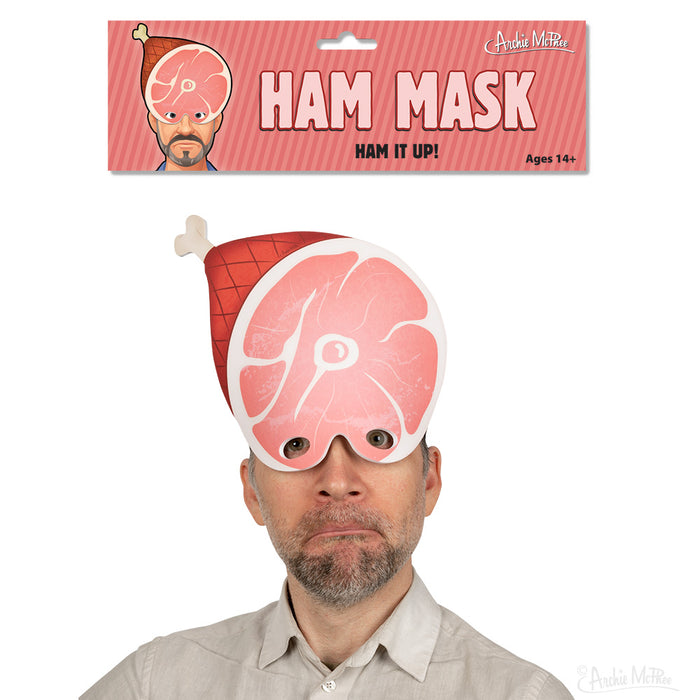 Ham Mask product packaging and demonstration image showing a person wearing a pink foam mask shaped like a slice of ham, with packaging text reading "HAM MASK" and "HAM IT UP!" Suitable for ages 14 and up.