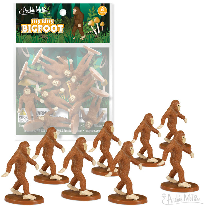 Itty Bitty Bigfoot toy set featuring 8 miniature Sasquatch figurines, each standing on a small base. Packaging shows forest-themed design with Bigfoot silhouette. Tiny brown Bigfoot figures displayed in various walking poses.