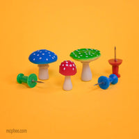 Three red, green and blue itty bitty mushrooms showing size compared to three push pins 