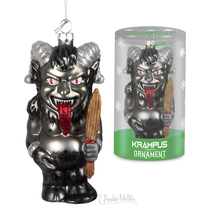 Hand-blown glass Krampus ornament with silver horns, red eyes, and tongue, holding a wooden stick. Displayed next to its packaging, a cylindrical box with snowflake design and green label reading "Krampus Ornament".