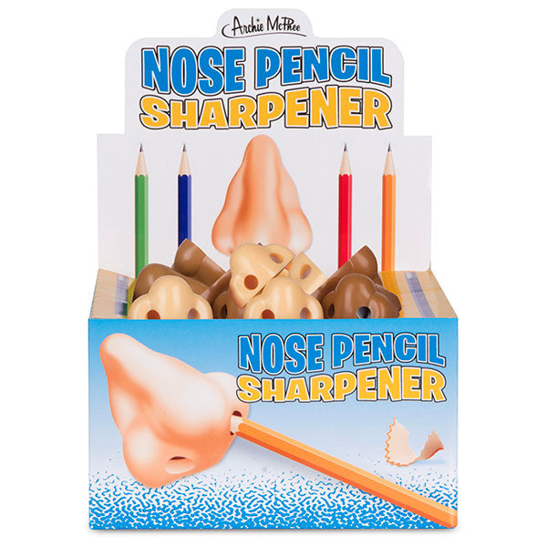 Nose-shaped pencil sharpeners in display box with colorful pencils. Product packaging shows nose with inserted pencil and shavings. Multiple sharpeners in different skin tones visible.