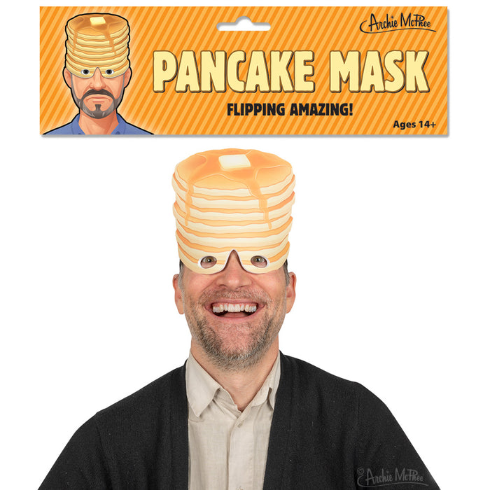 Pancake Mask product image showing a smiling person wearing a novelty mask resembling a stack of pancakes with butter on top, packaged in orange-striped cardboard with "PANCAKE MASK" and "FLIPPING AMAZING!" text