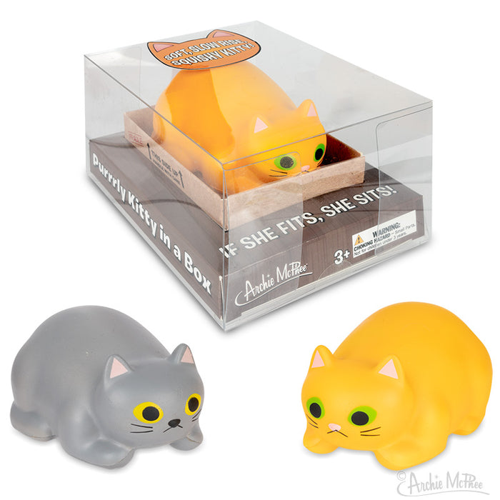 Purrrly Kitty stress relief toys: Yellow and gray cat-shaped squeezable foam figures in cardboard box. Product packaging shows clear plastic display with orange logo. Cats have wide eyes and cute expressions, designed for stress relief and easy storage.