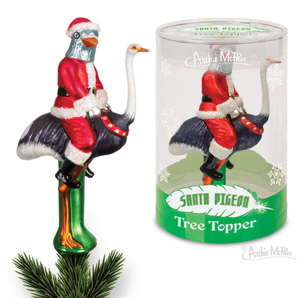 Whimsical glass tree topper featuring Santa with a pigeon head riding an ostrich, displayed next to its packaging. The ornament stands on a green base with pine needles, showcasing its unique and quirky holiday design.