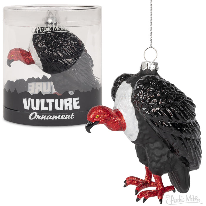 Glass vulture Christmas ornament with red Santa hat and feet, packaged in clear tube. Black bird with detailed feathers and white neck ruff, perched in festive pose. Unique holiday decoration for nature lovers.