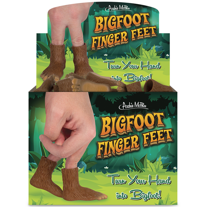 Bigfoot Finger Feet product display box featuring miniature hairy feet worn on fingers, set against a forest background. The packaging showcases the product in use, with hands demonstrating how to wear the tiny Bigfoot feet on fingertips, transforming hands into playful Sasquatch appendages.