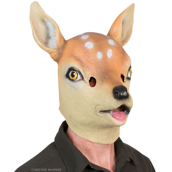 Realistic latex deer mask with large eyes, spotted fur, and pointed ears, worn by figure in dark jacket, creating whimsical woodland creature appearance for costume or roleplay