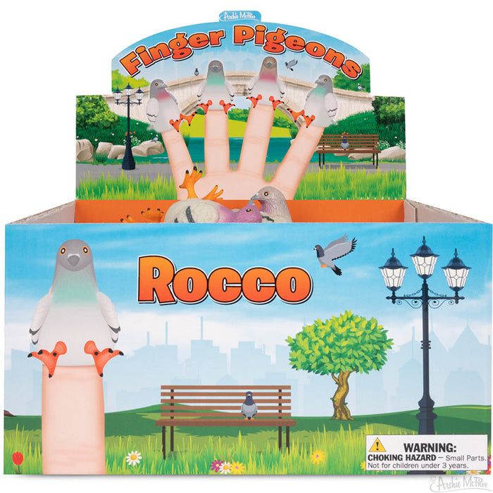 Colorful display box of Finger Pigeons vinyl puppets showcasing four different shades on a hand against a park backdrop with trees, bench, and lamppost. Includes product name and choking hazard warning.