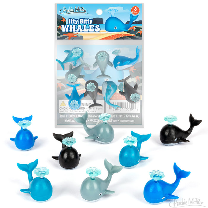 Colorful miniature whale toys in various shades of blue and black, with water sprays from blowholes. Eight small vinyl whales displayed outside packaging, showing product variety. Packaging visible with "Itty Bitty Whales" branding and quantity information.