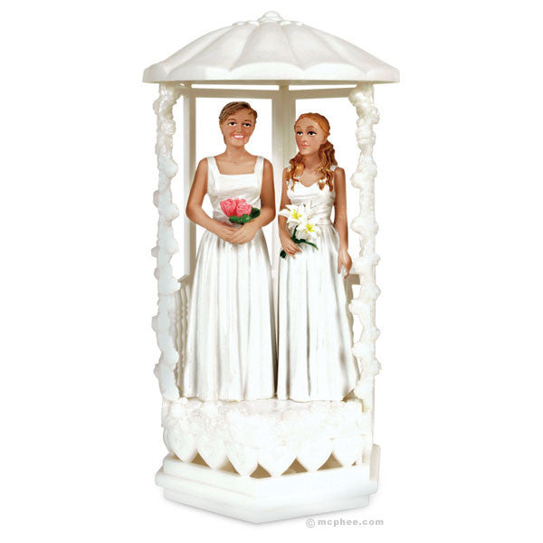 Two brides wedding cake topper featuring figures in white dresses standing in a decorative white gazebo, holding bouquets. One bride has short hair, the other has long hair. The topper is made of plastic and stands about 6.5 inches tall.