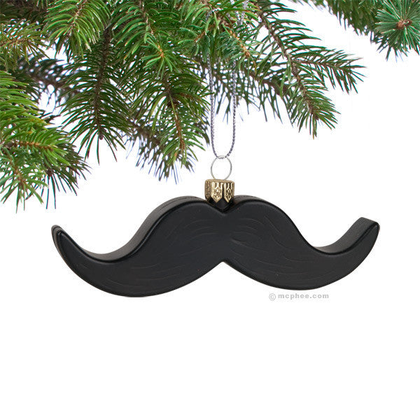 Black mustache-shaped Christmas ornament hanging from green pine tree branch, adding a whimsical and gentlemanly touch to holiday decor