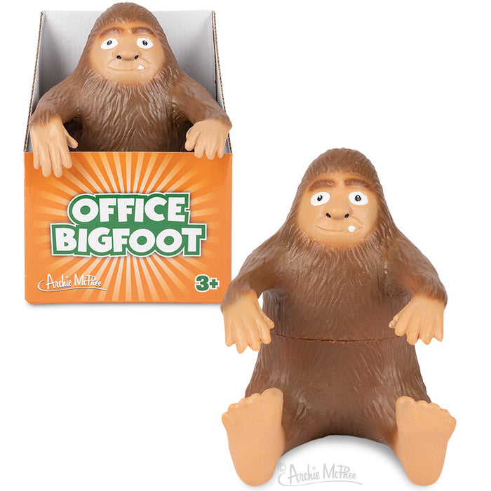 Office Bigfoot toy, a brown furry creature with wide eyes and friendly expression, sitting in and next to an orange packaging box. The posable figure has large hands and feet, perfect for desktop companionship and stress relief in the workplace.