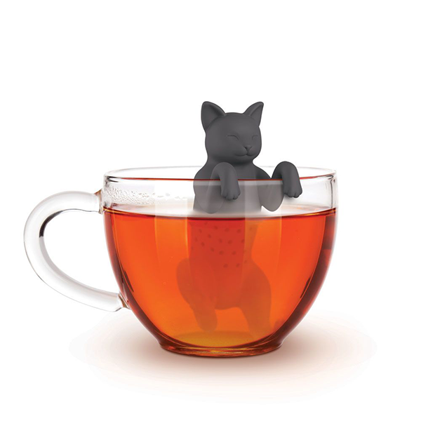 Cat-shaped tea infuser hanging on clear glass cup filled with orange tea. Gray silicone cat figure rests on cup rim, its body submerged in the tea as an infuser.