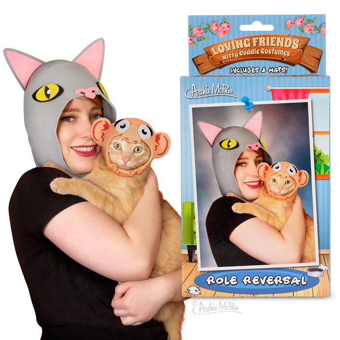 Person wearing cat costume hat holding cat wearing human costume hat, with product packaging showing "Loving Friends Kitty Cuddle Costumes: Role Reversal" for humorous pet and owner photo opportunities