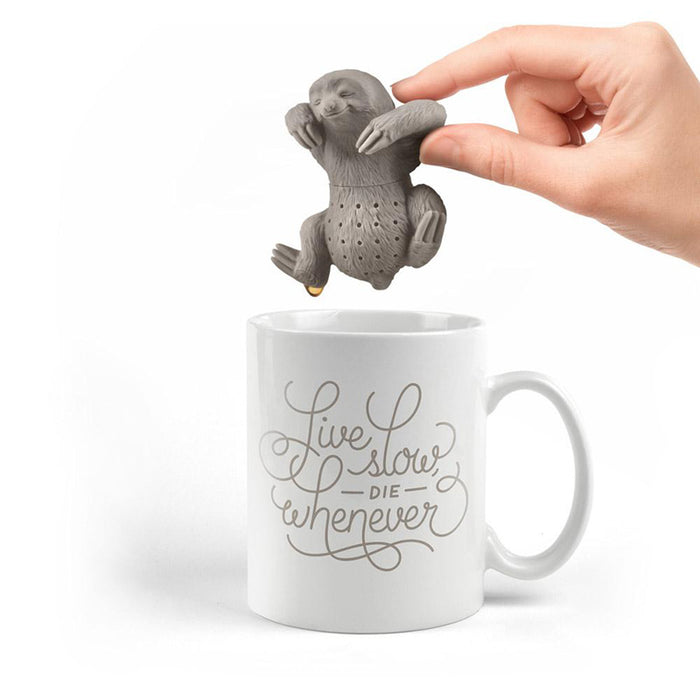 Cute sloth-shaped tea infuser held over a white mug with inspirational text. The silicone sloth has perforations for steeping tea and is being gently gripped by a human hand, demonstrating its use as a unique and whimsical tea steeper.